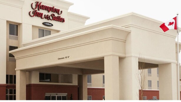 A Hampton Inn & Suites hotel with a clear sign, a flag, and a 'Clearance 16'-0"' marking on the building facade.