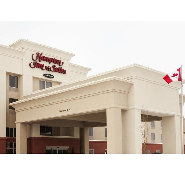 Un hotel Hampton Inn & Suites con un letrero visible, una bandera y la indicación 'Clearance 16'-0"' en la fachada.