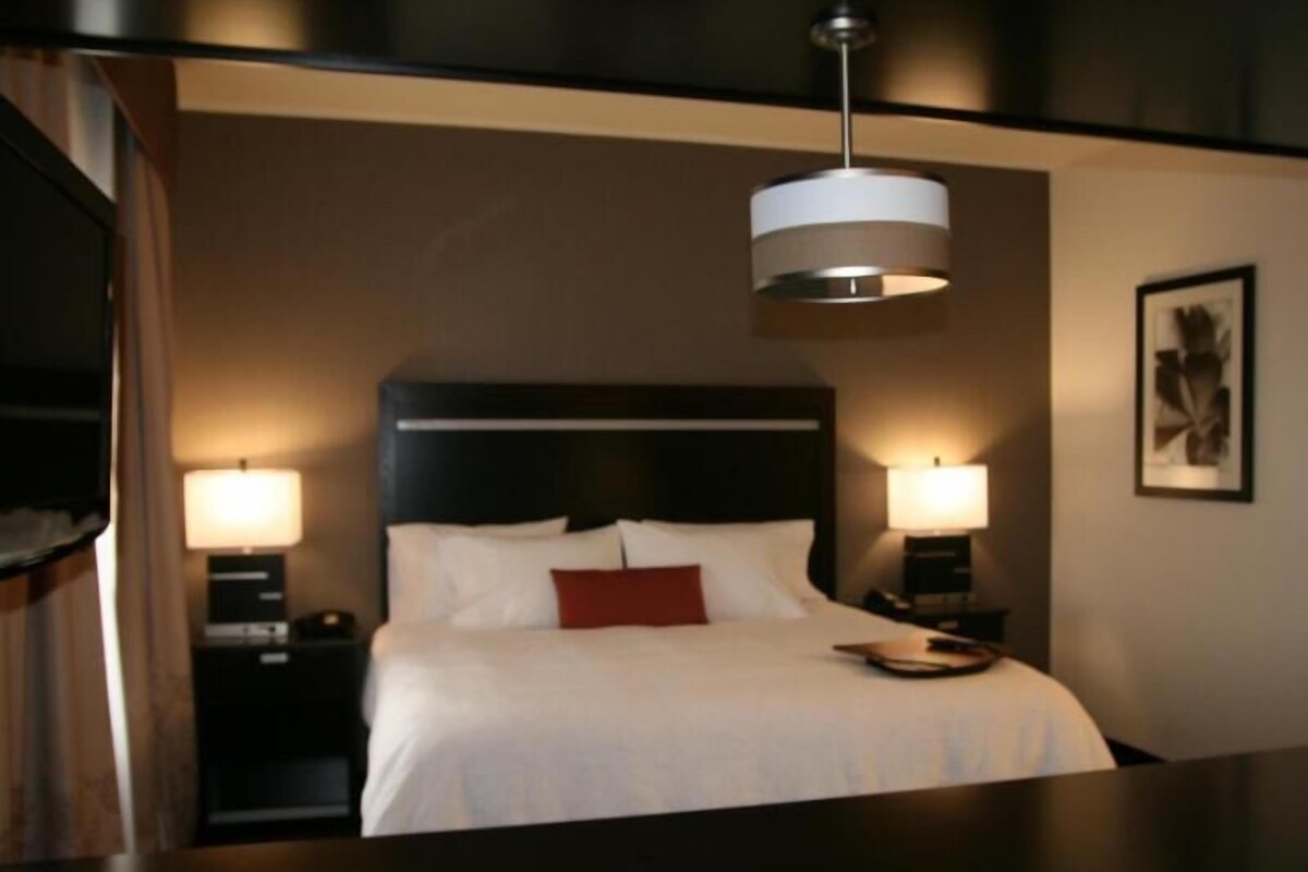 Una habitación de hotel con cama, lámparas de noche, una mesita de noche y una lámpara de pared.