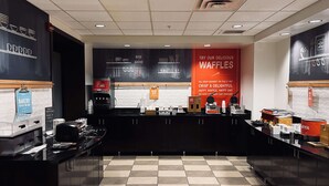A bakery counter with a sign promoting waffles, a coffee machine, and a menu board.