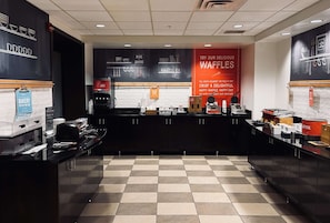 A bakery counter with a sign promoting waffles, a coffee machine, and a menu board.