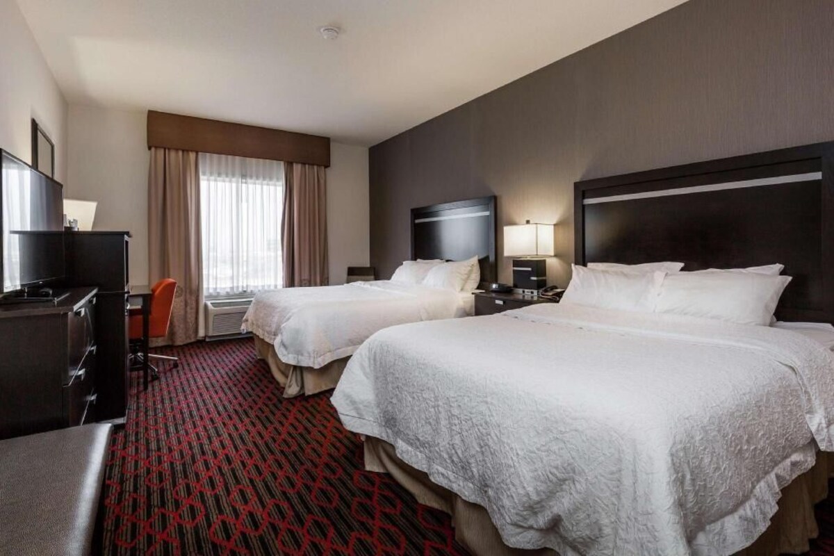 Habitación de hotel con dos camas, un escritorio, una silla, un televisor y una ventana con cortinas.