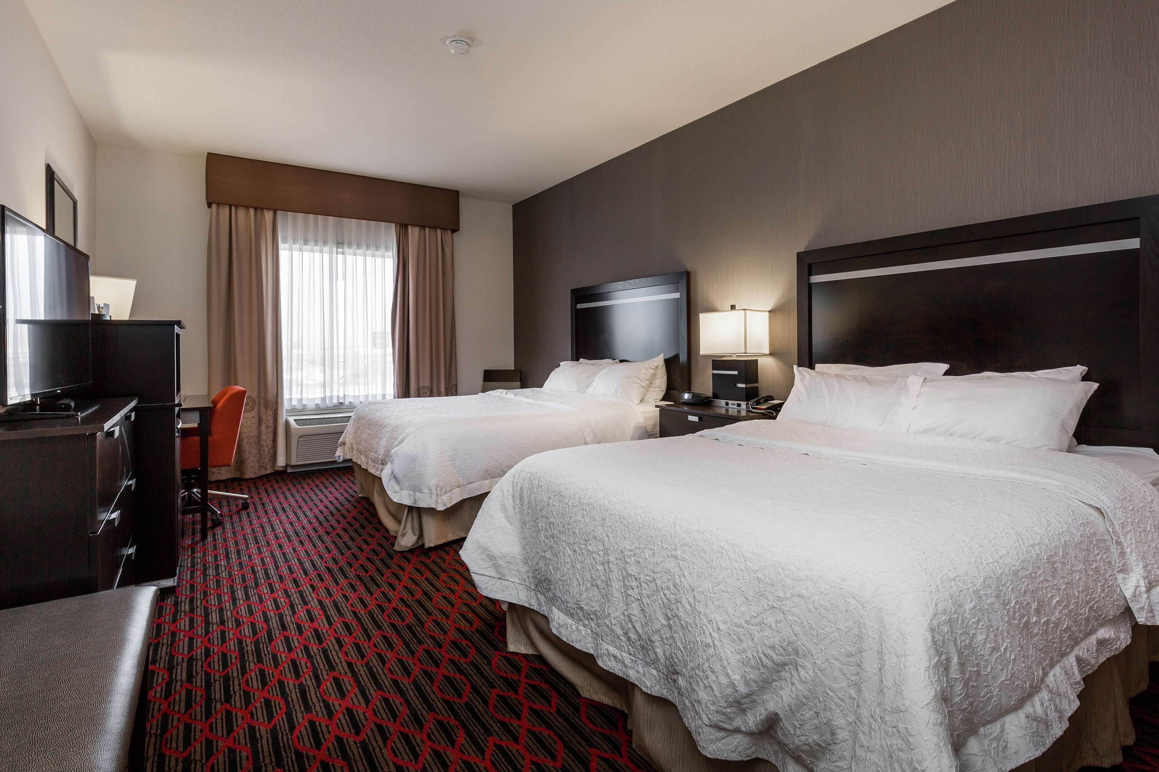 A hotel room with two beds, a desk, a chair, a TV, and a window with curtains.