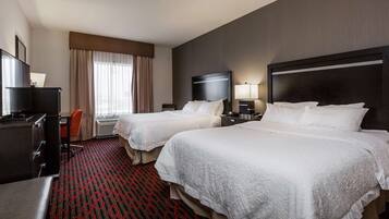 Habitación de hotel con dos camas, un escritorio, una silla, un televisor y una ventana con cortinas.