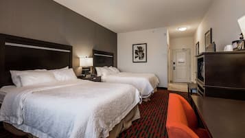 Habitación de hotel con dos camas, un escritorio y una silla. Se ve un aparador y una puerta al fondo.