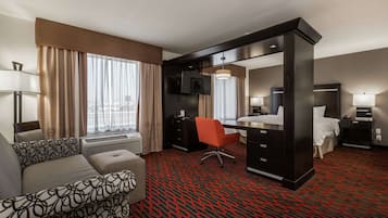 Habitación de hotel con sofá, escritorio, silla, cama, televisor y ventana con cortinas.