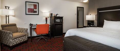 Une chambre d’hôtel avec un grand lit, un bureau avec une chaise, un four à micro-ondes et deux lampes.