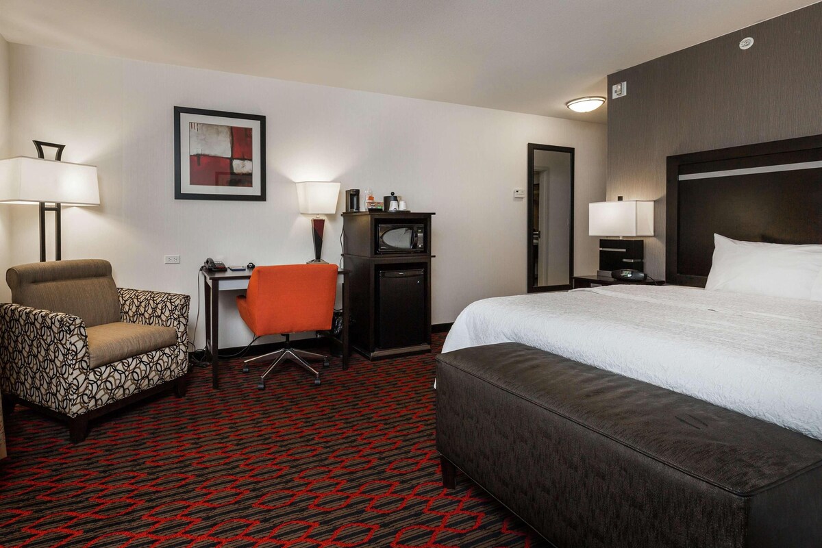 Una habitación de hotel con cama, dos sillas, escritorio, microondas y lámpara.