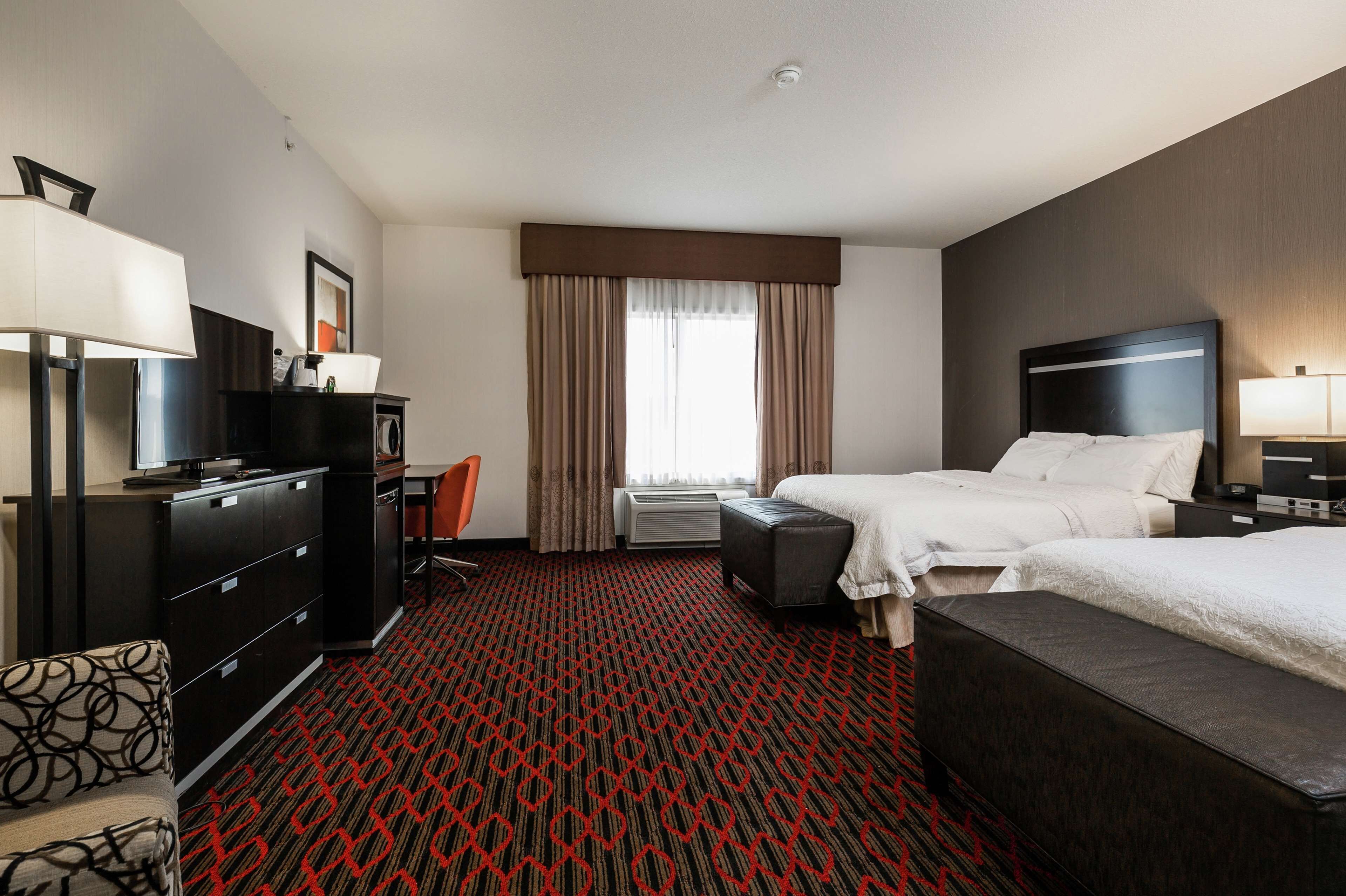 A hotel room with a large bed, a desk with a chair, a television, and a wardrobe.