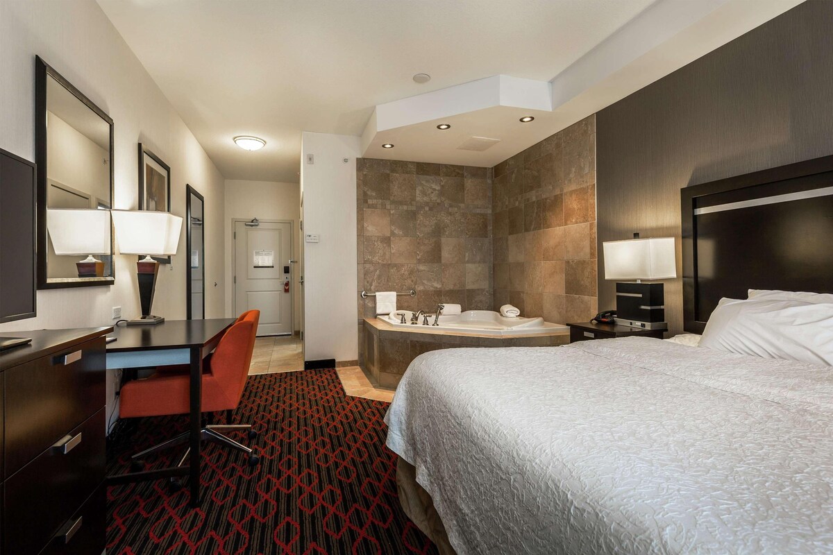 Una habitación de hotel con cama, escritorio, silla y baño con bañera y lavamanos.