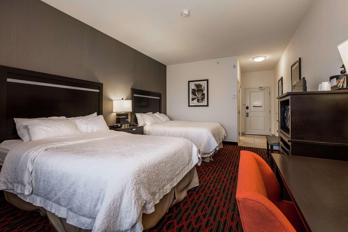 Una habitación de hotel con dos camas, un escritorio, una silla y un aparador.