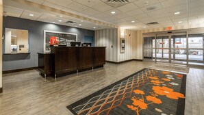 Zona de recepción de un hotel con mostrador, pantalla digital y alfombra estampada con motivos florales.