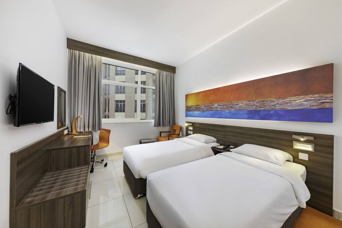 A hotel room with two beds, a desk, a TV, and a painting on the wall.