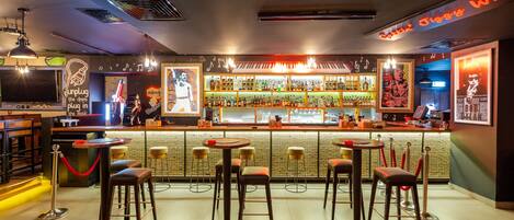 Um bar com vários bancos, um balcão com diversas garrafas e um letreiro de neon.