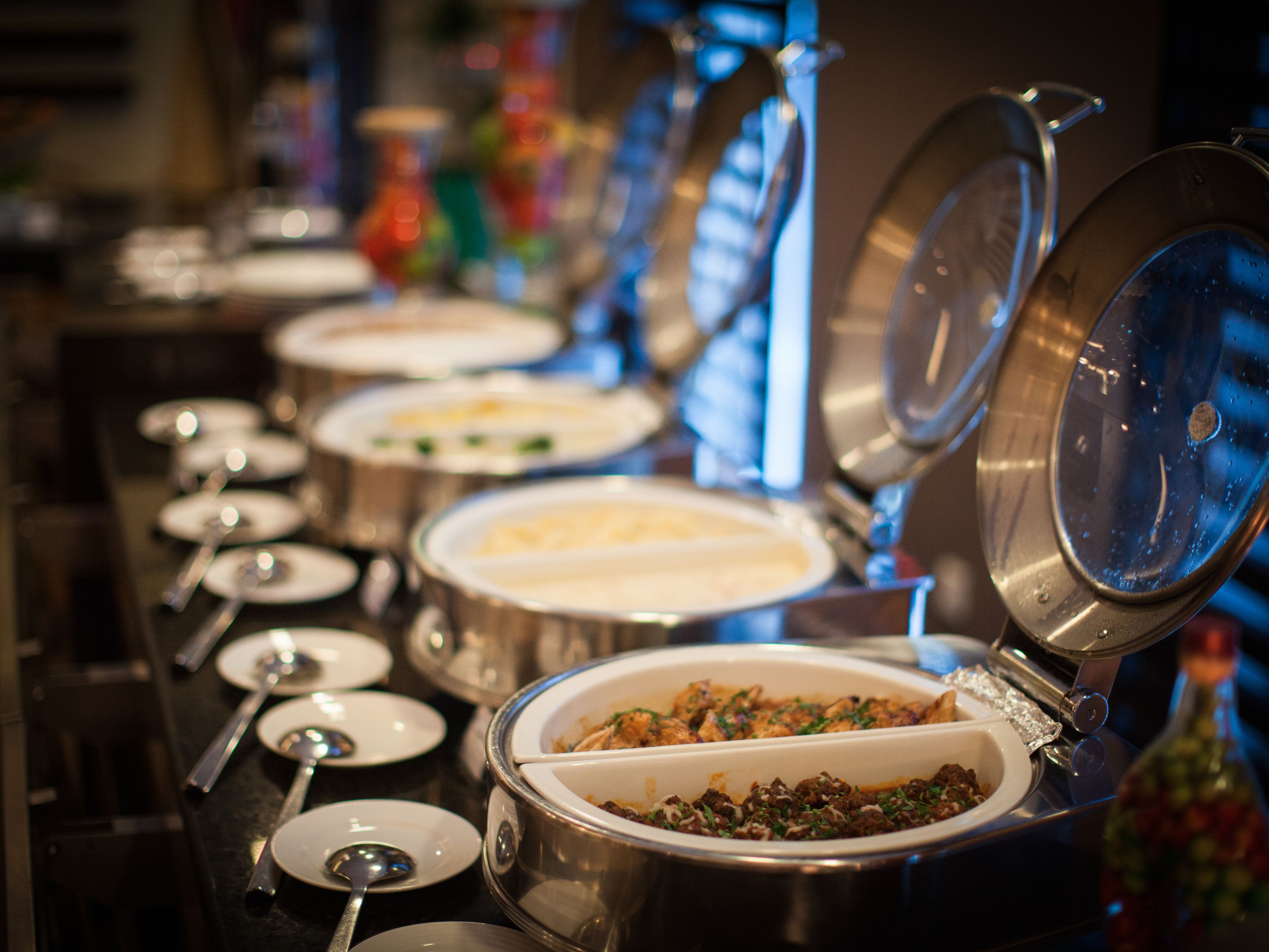 A buffet line with various dishes in metal serving containers, some with lids open.