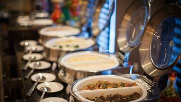 A buffet line with various dishes in metal serving containers, some with lids open.