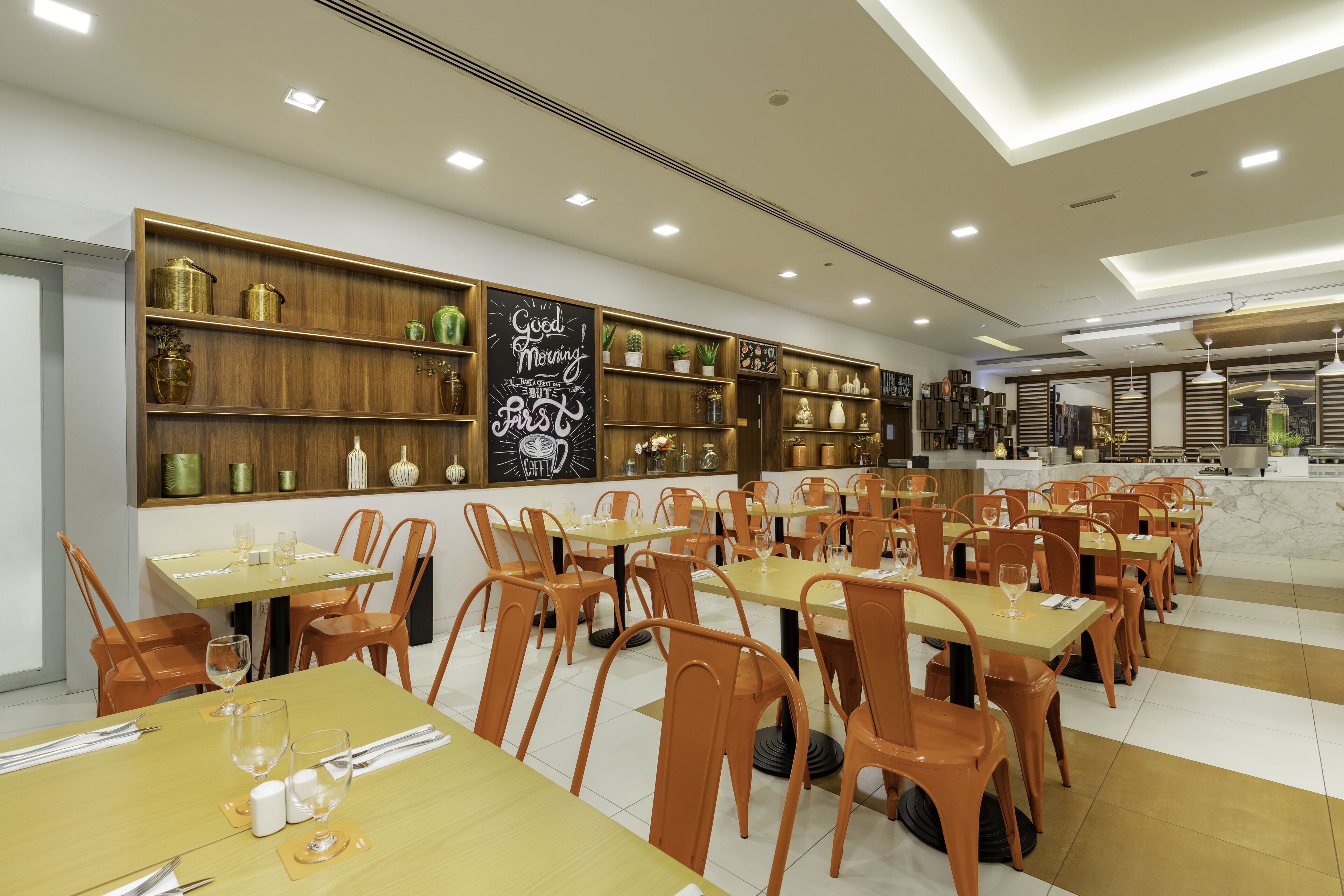 A modern restaurant with wooden shelves, orange chairs, and tables set for dining.