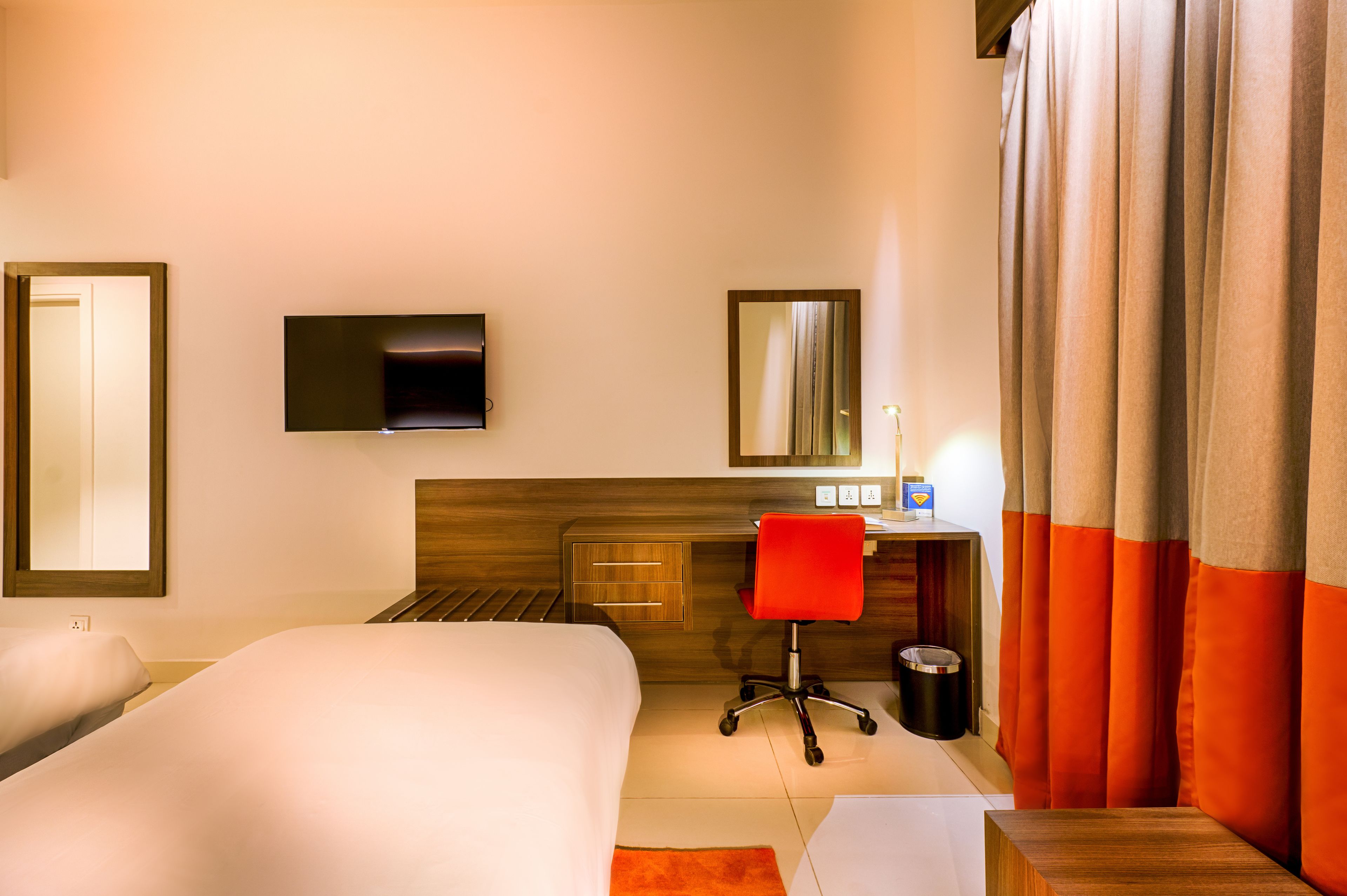 Ein Hotelzimmer mit Bett, Schreibtisch mit Stuhl, Fernseher und Vorhängen.