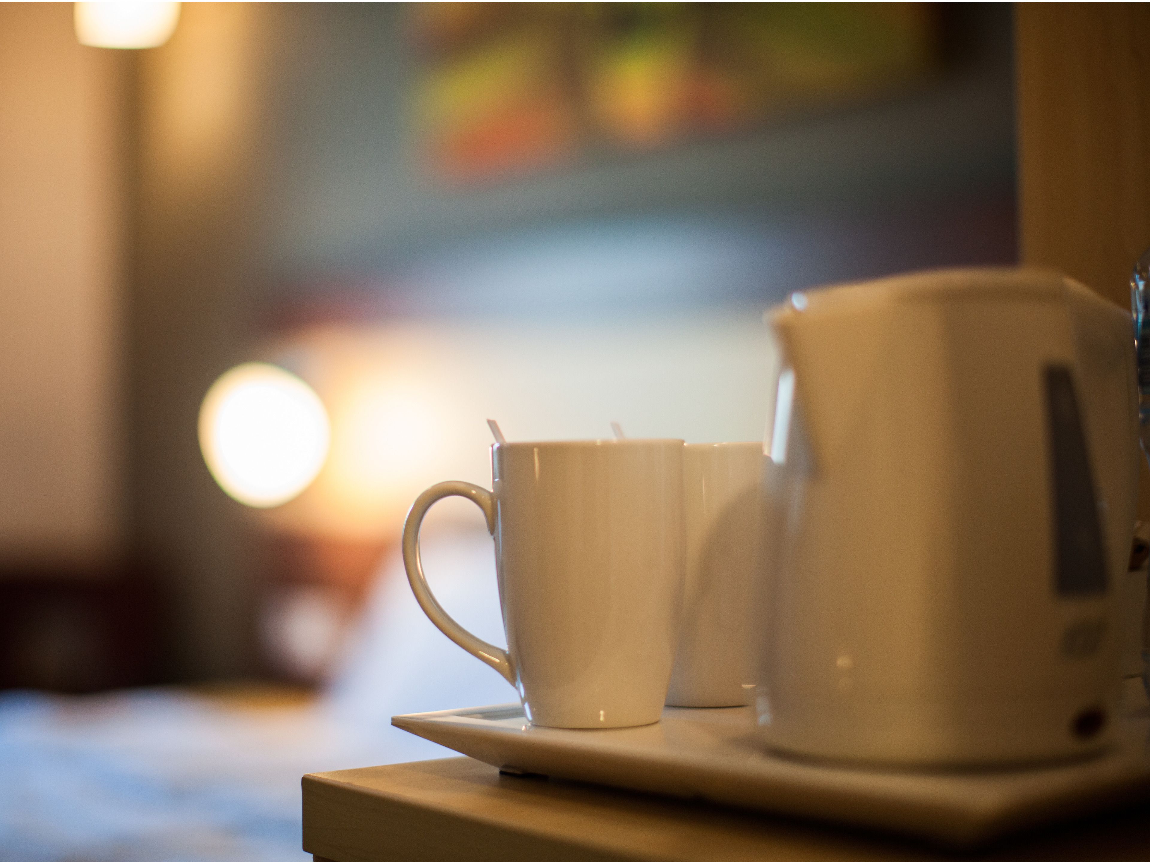 A white coffee cup and a white teapot on a tray.