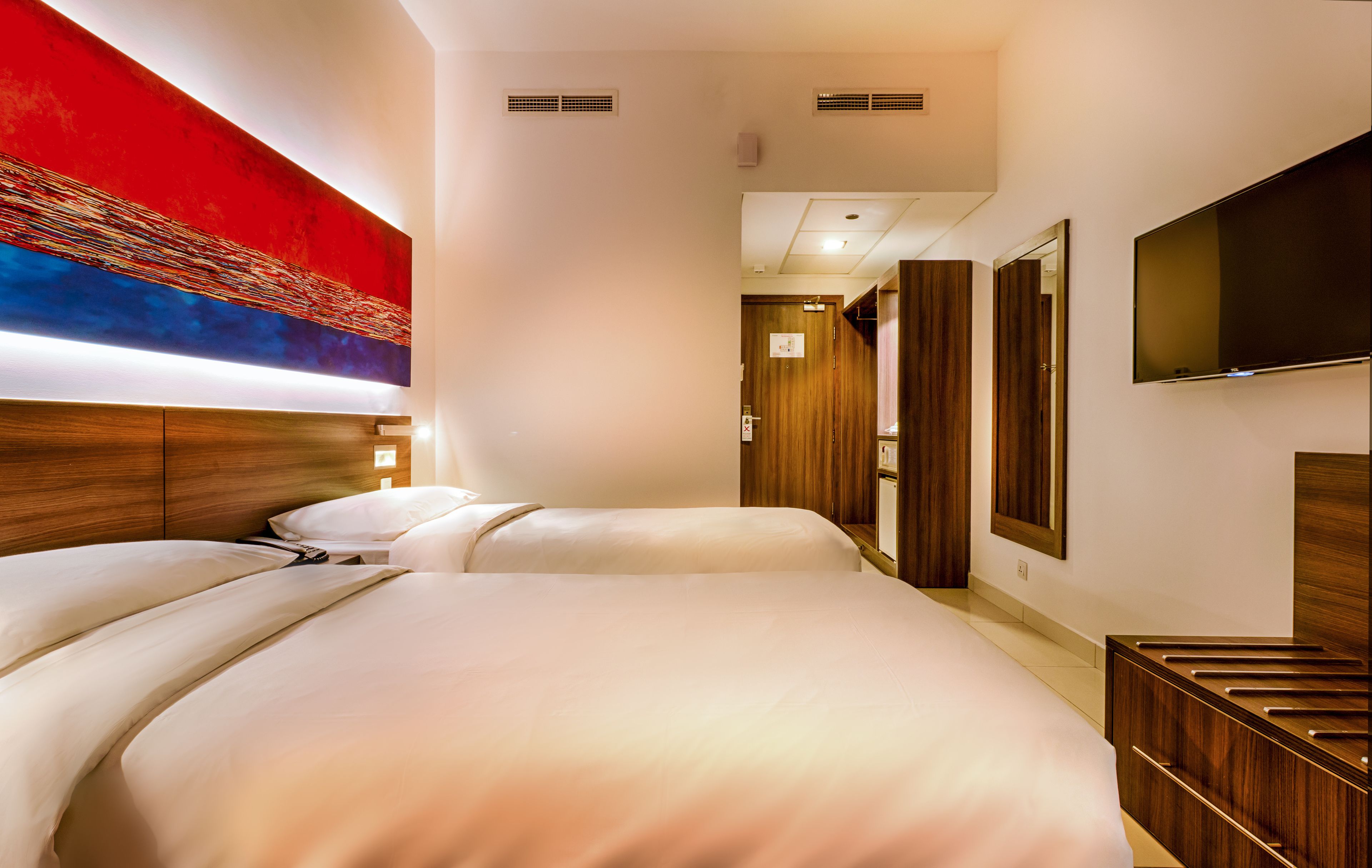 A hotel room with two beds, a large abstract painting on the wall, a flat-screen TV, and a wooden headboard.
