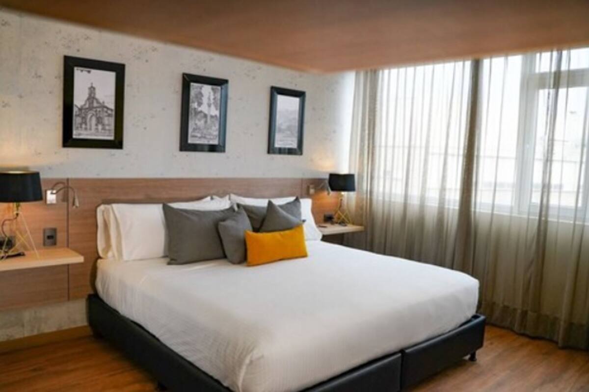 Ein Hotelzimmer mit einem großen Bett, zwei Nachttischen mit Lampen, einem Holz-Kopfteil und drei gerahmten Bildern an der Wand.