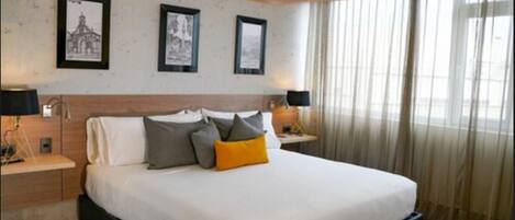 A hotel room with a large bed, two bedside tables with lamps, a wooden headboard, and three framed pictures on the wall.