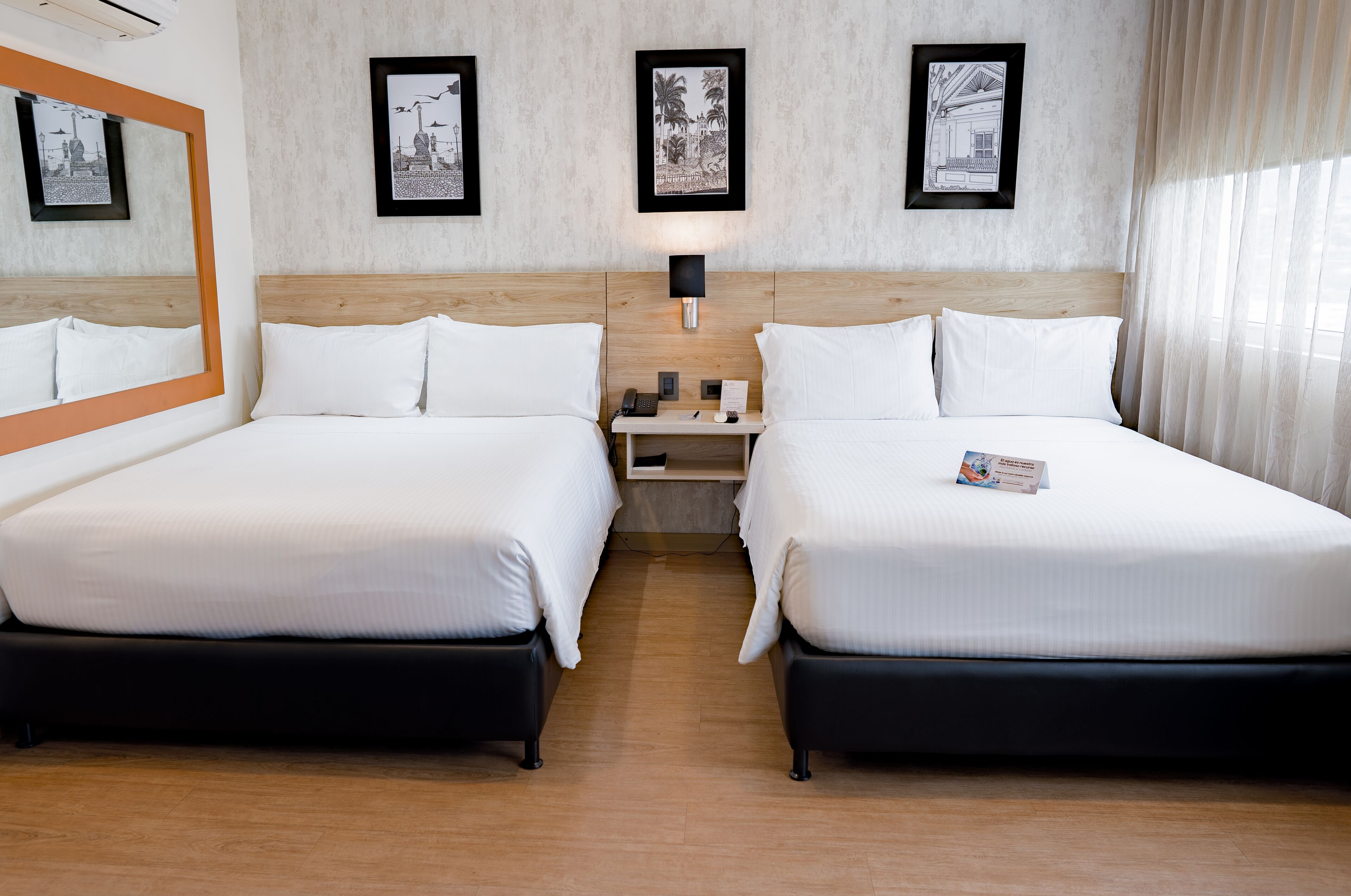 Ein Hotelzimmer mit zwei Betten, einem Nachttisch, einer Lampe und gerahmten Bildern an der Wand.