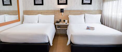 Ein Hotelzimmer mit zwei Betten, einem Nachttisch, einer Lampe und gerahmten Bildern an der Wand.