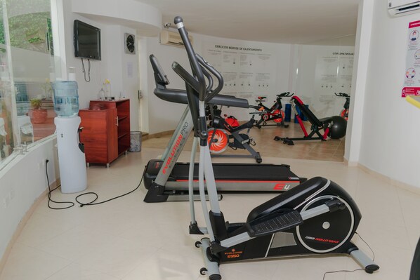 Un gimnasio en casa con bicicletas estáticas, cintas de correr y un dispensador de agua.
