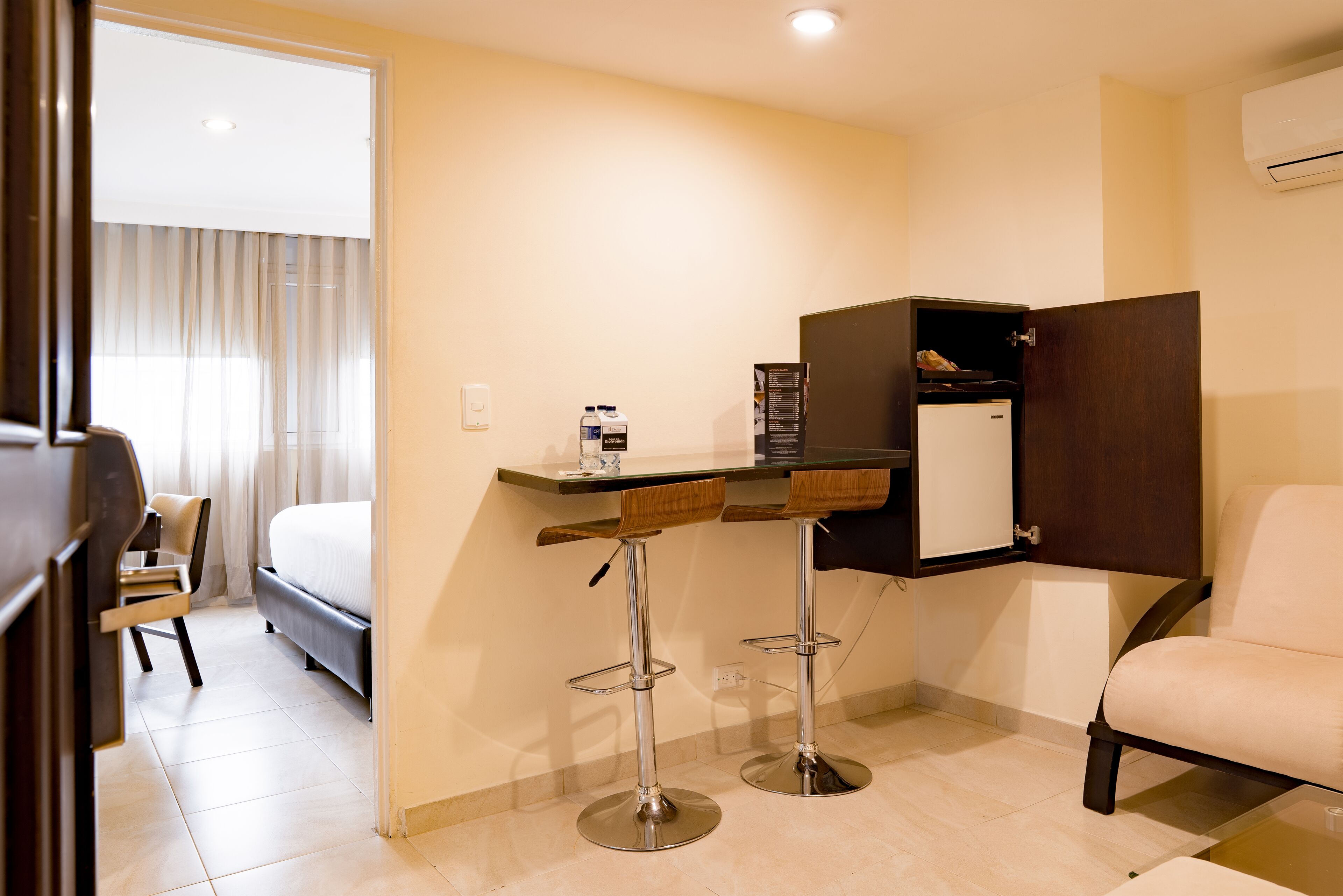 Ein Hotelzimmer mit einem Bett, einem Schreibtisch mit zwei Hocker, einem Sessel, einem Kleiderschrank und einem kleinen Kühlschrank.
