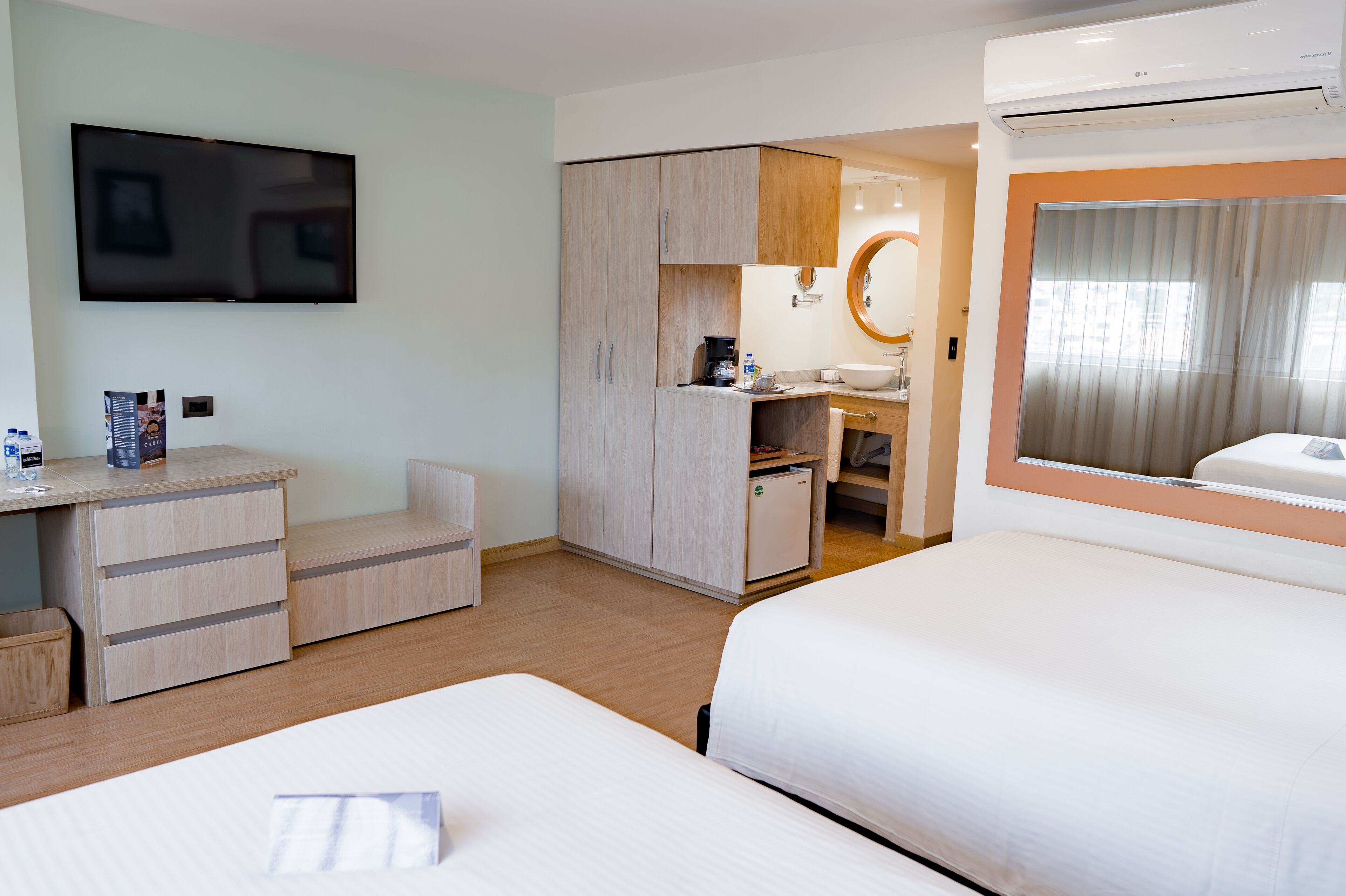 Une chambre d’hôtel équipée d’une télévision, d’un bureau avec des tiroirs, d’un lit, d’une petite kitchenette et d’une salle de bain avec un miroir.
