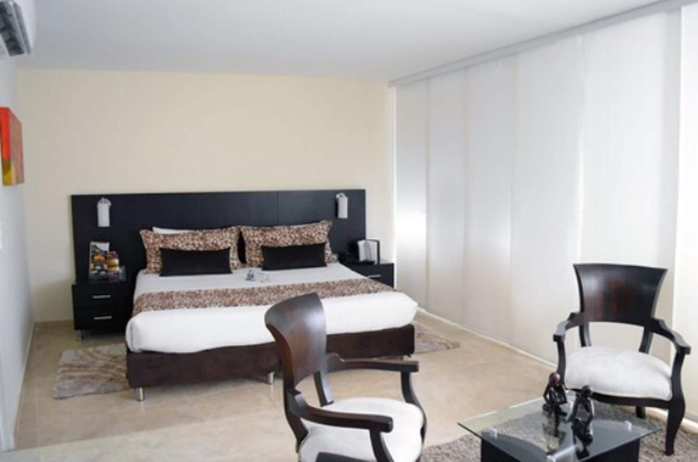 A bedroom with a large bed, two nightstands, a chair, and a small table.