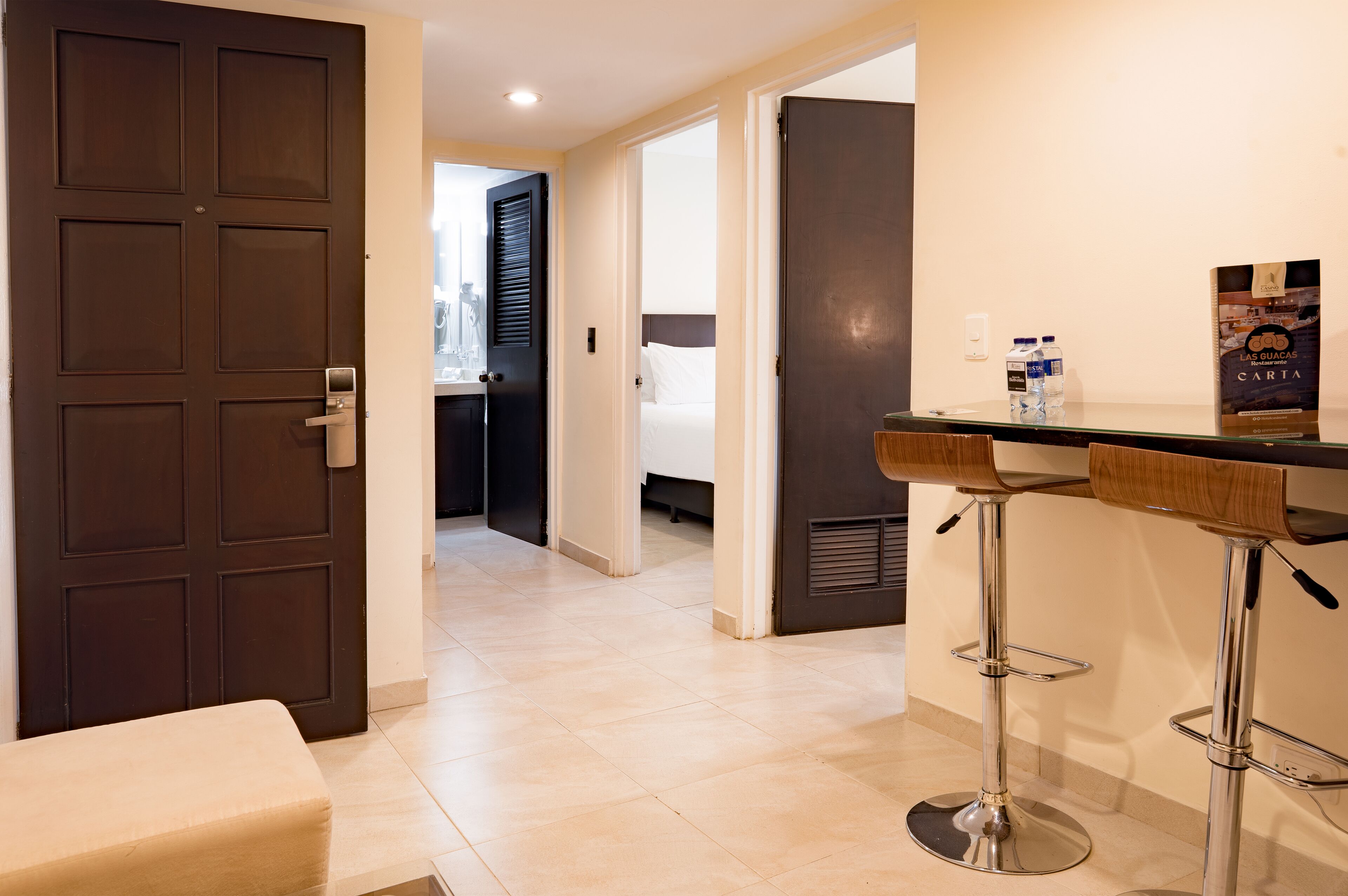 A hotel room with a dark wooden door, a small seating area, and a bar with stools.