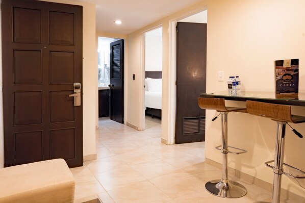 A hotel room with a dark wooden door, a small seating area, and a bar with stools.