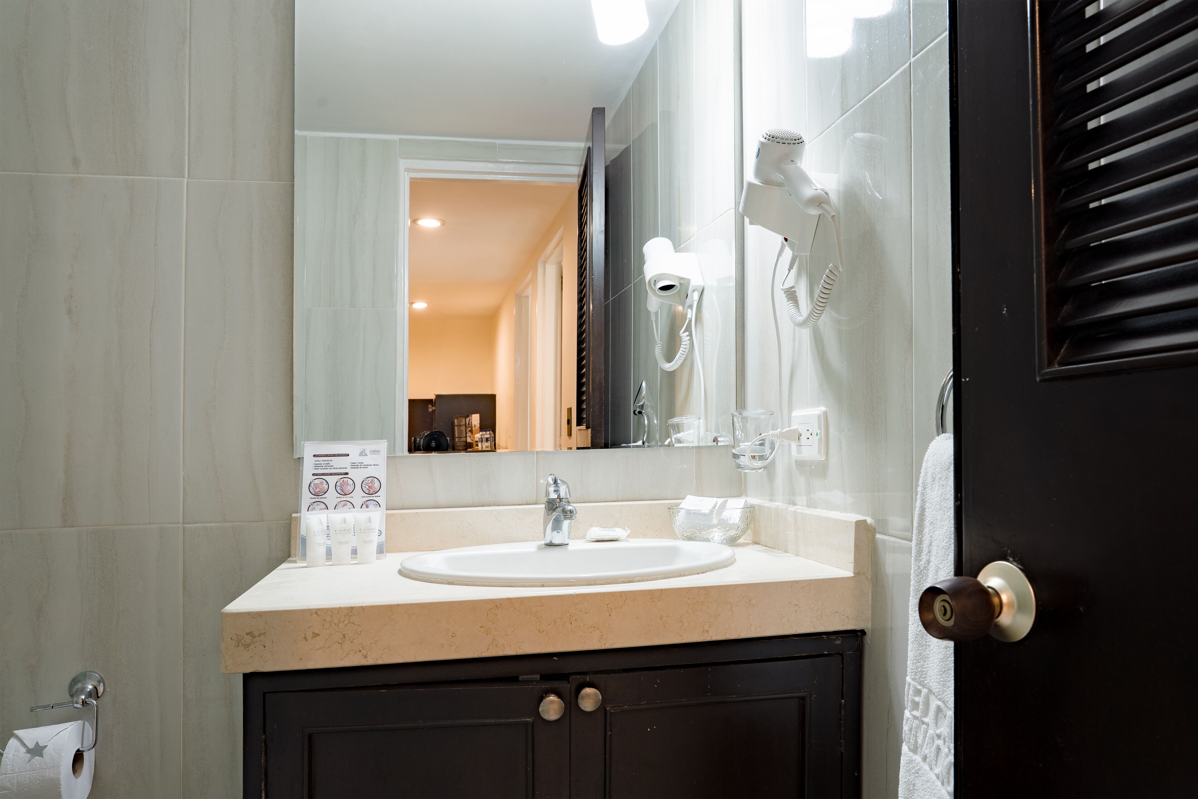 Une salle de bain équipée d’un lavabo, d’un miroir, d’un sèche-cheveux et d’un porte-serviettes.