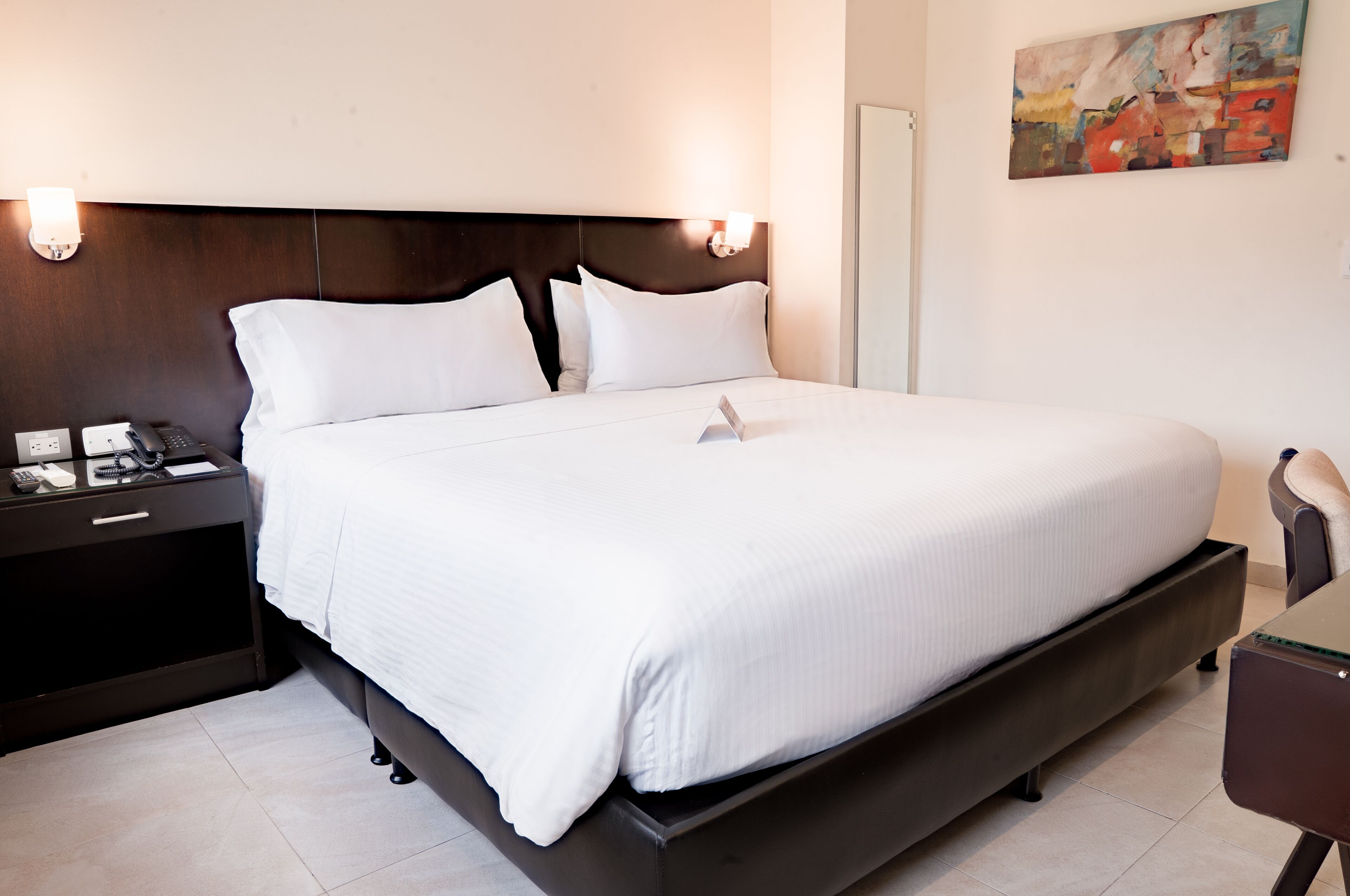 Een hotelkamer met een groot bed, nachtkastjes, een telefoon en een schilderij aan de muur.