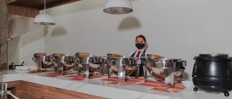 A buffet setup with multiple serving bowls and a large pot, set against a marble countertop and wooden ceiling beams.