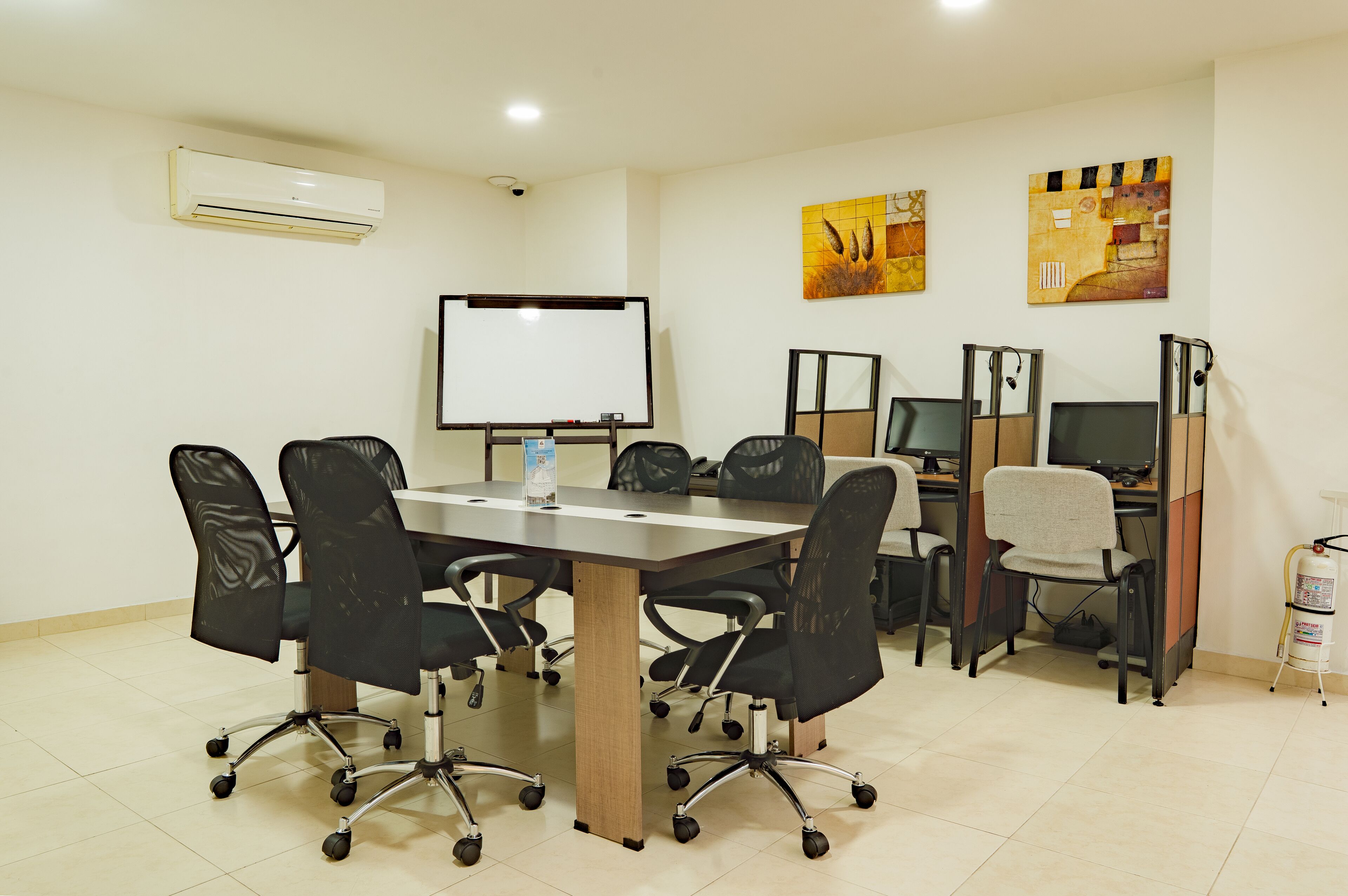 A conference room with a large table, black office chairs, a whiteboard, two computer monitors, and artwork on the walls.