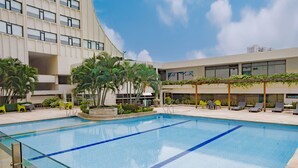 A swimming pool with clear blue water, surrounded by lounge chairs and a building with large windows and balconies.