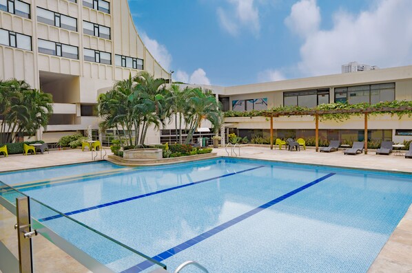 A swimming pool with clear blue water, surrounded by lounge chairs and a building with large windows and balconies. - Hotel Casino Internacional (San José de Cúcuta)