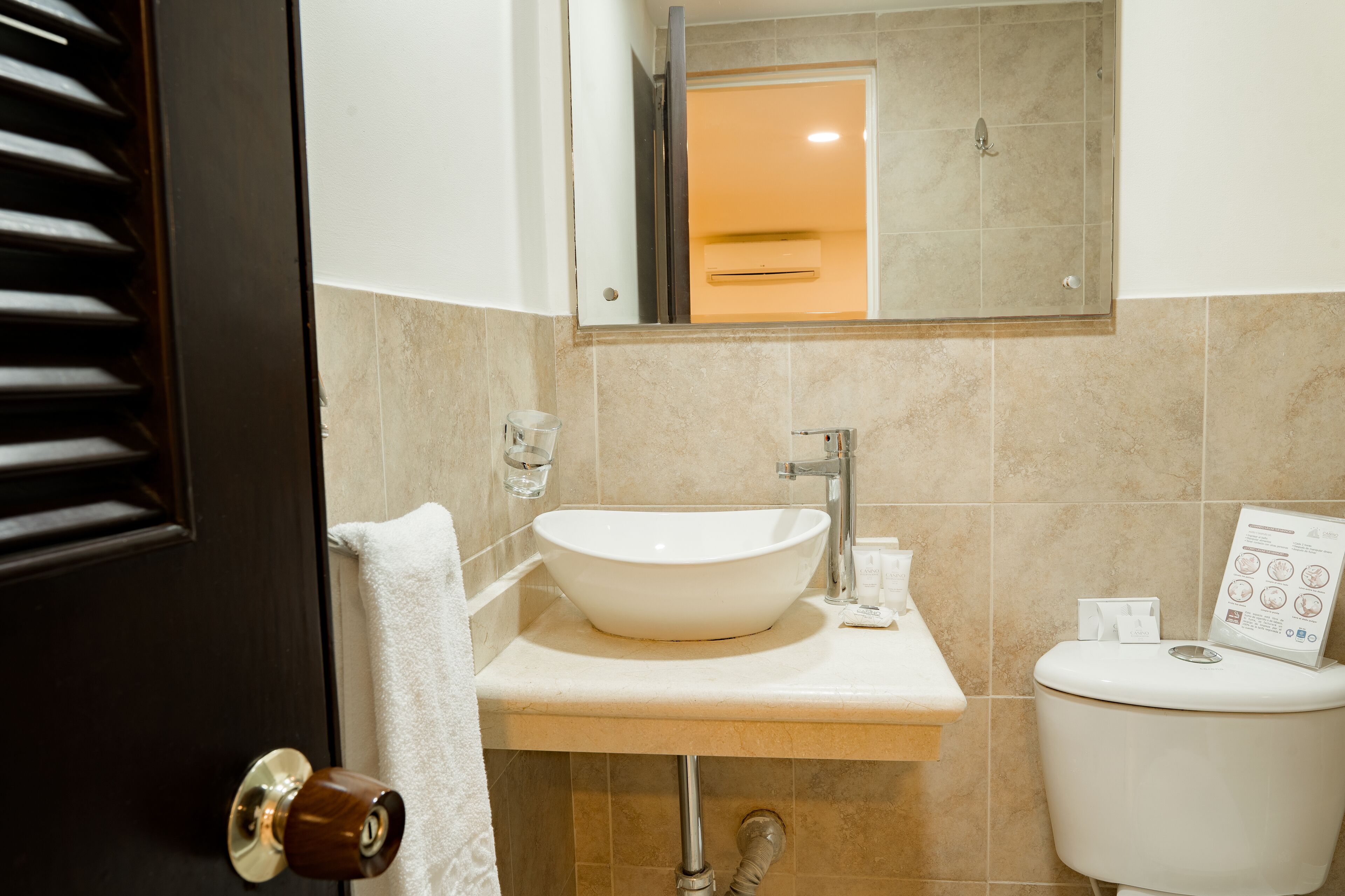 A bathroom with a white sink, a mirror, a toilet, and a towel hanging on the door.