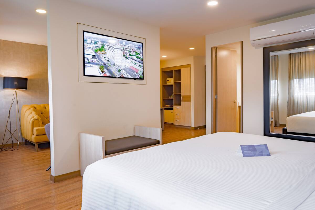 Ein Hotelzimmer mit Bett, Wandfernseher, Sofa und Schreibtisch mit Stuhl.