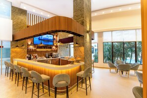 A bar area with a curved wooden counter, bar stools, a television, and a view of palm trees through large windows.