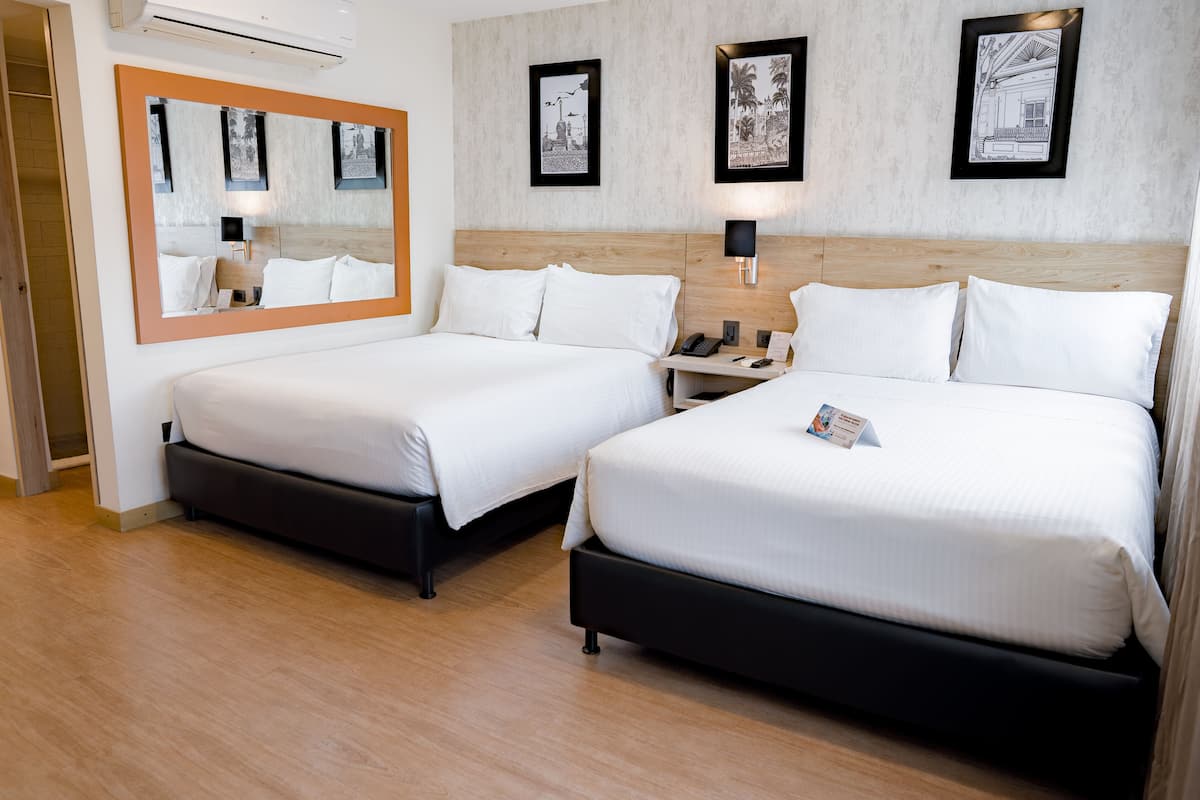 Ein Hotelzimmer mit zwei Betten, einem großen Spiegel, gerahmten Bildern, einem Nachttisch mit Lampe und Holzboden.