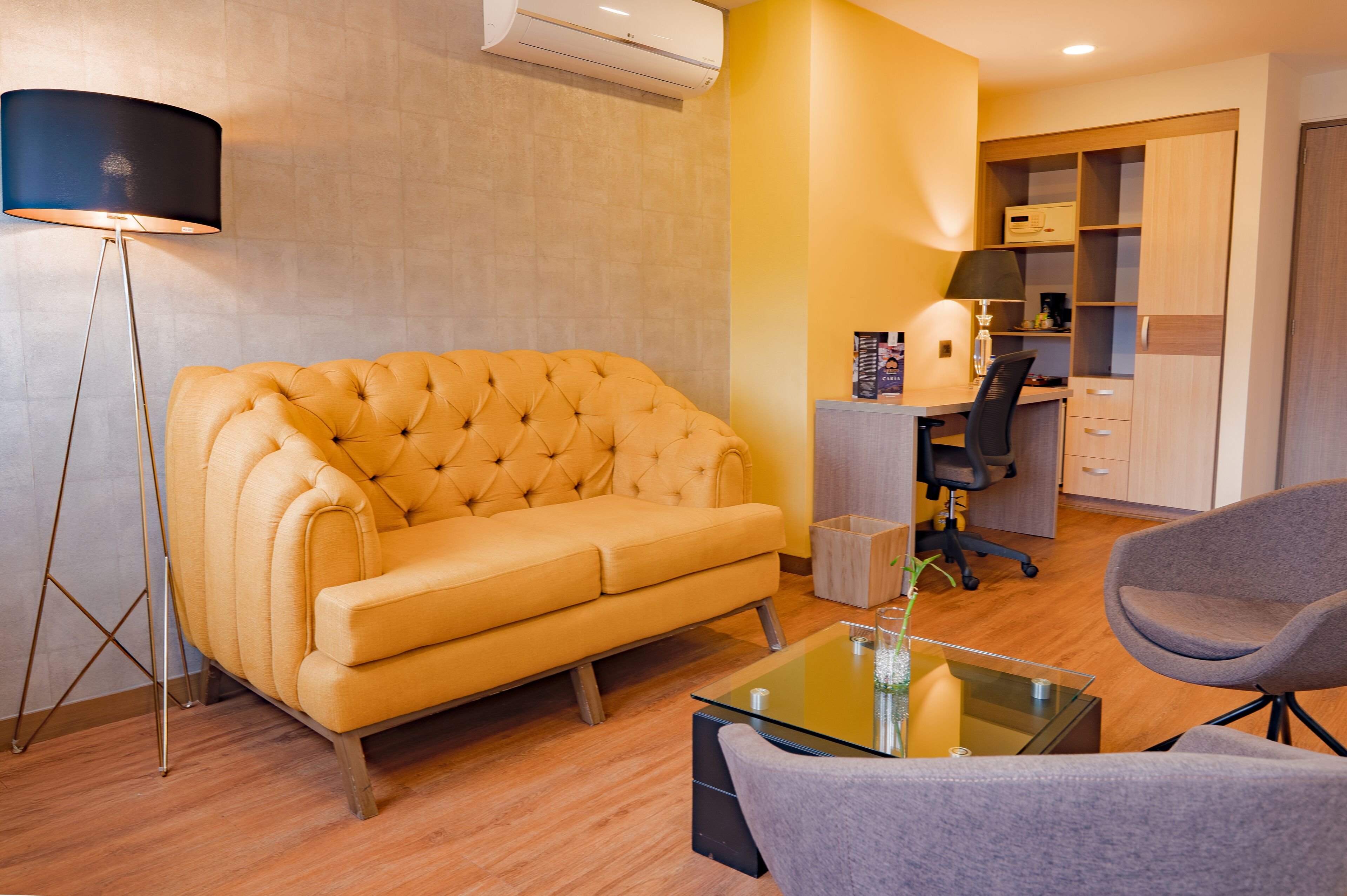 Un salon moderne avec un canapé capitonné, une table basse en verre, un lampadaire, un bureau avec une chaise et une armoire intégrée.