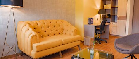 Un salon moderne avec un canapé capitonné, une table basse en verre, un lampadaire, un bureau avec une chaise et une armoire intégrée.