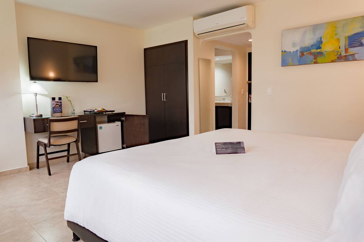 Ein Hotelzimmer mit Bett, Schreibtisch, Stuhl, Fernseher und Klimaanlage.