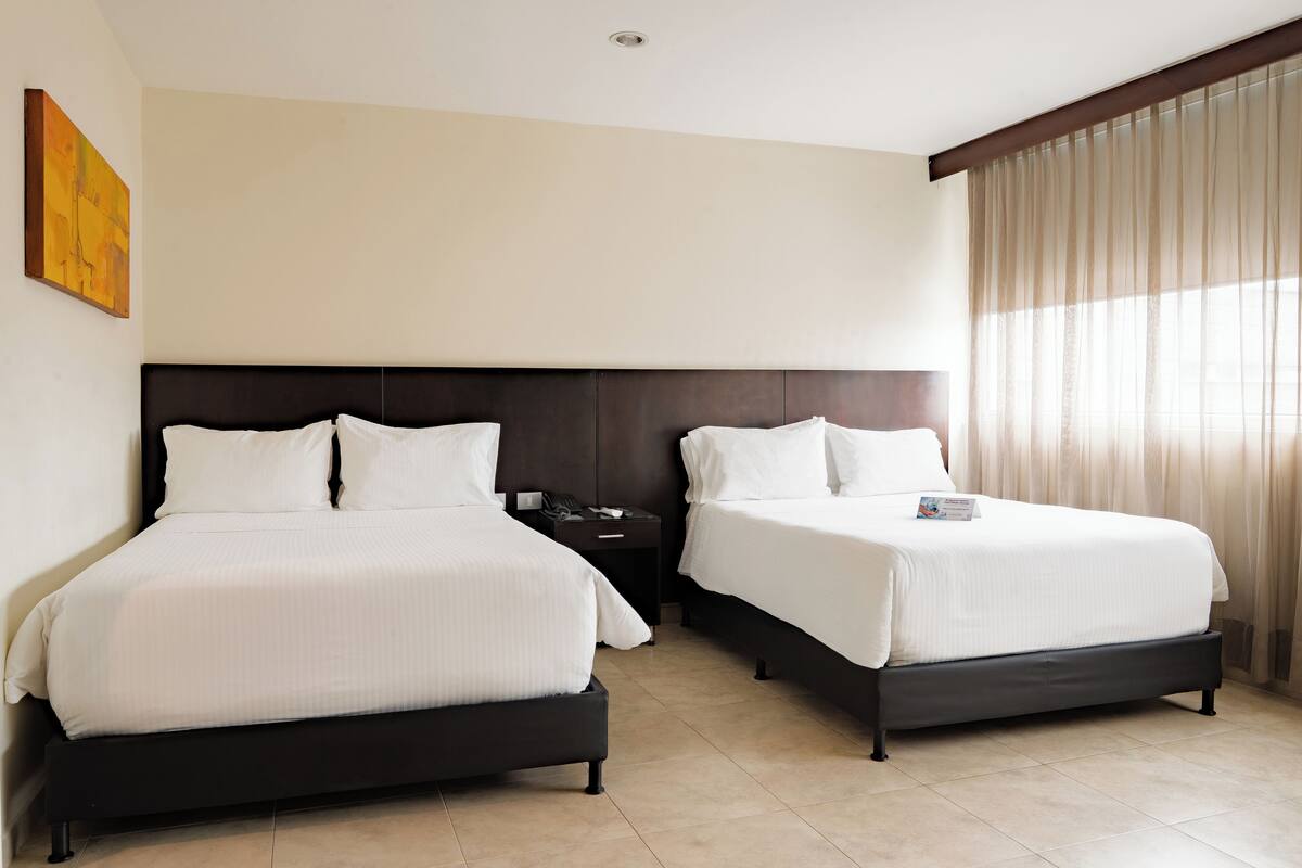 Ein Hotelzimmer mit zwei Betten, einem Nachttisch und einem Fenster mit Vorhängen.