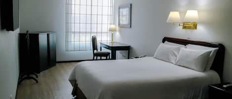 Habitación de hotel con una cama grande, un escritorio con silla, un televisor y dos lámparas de pared.