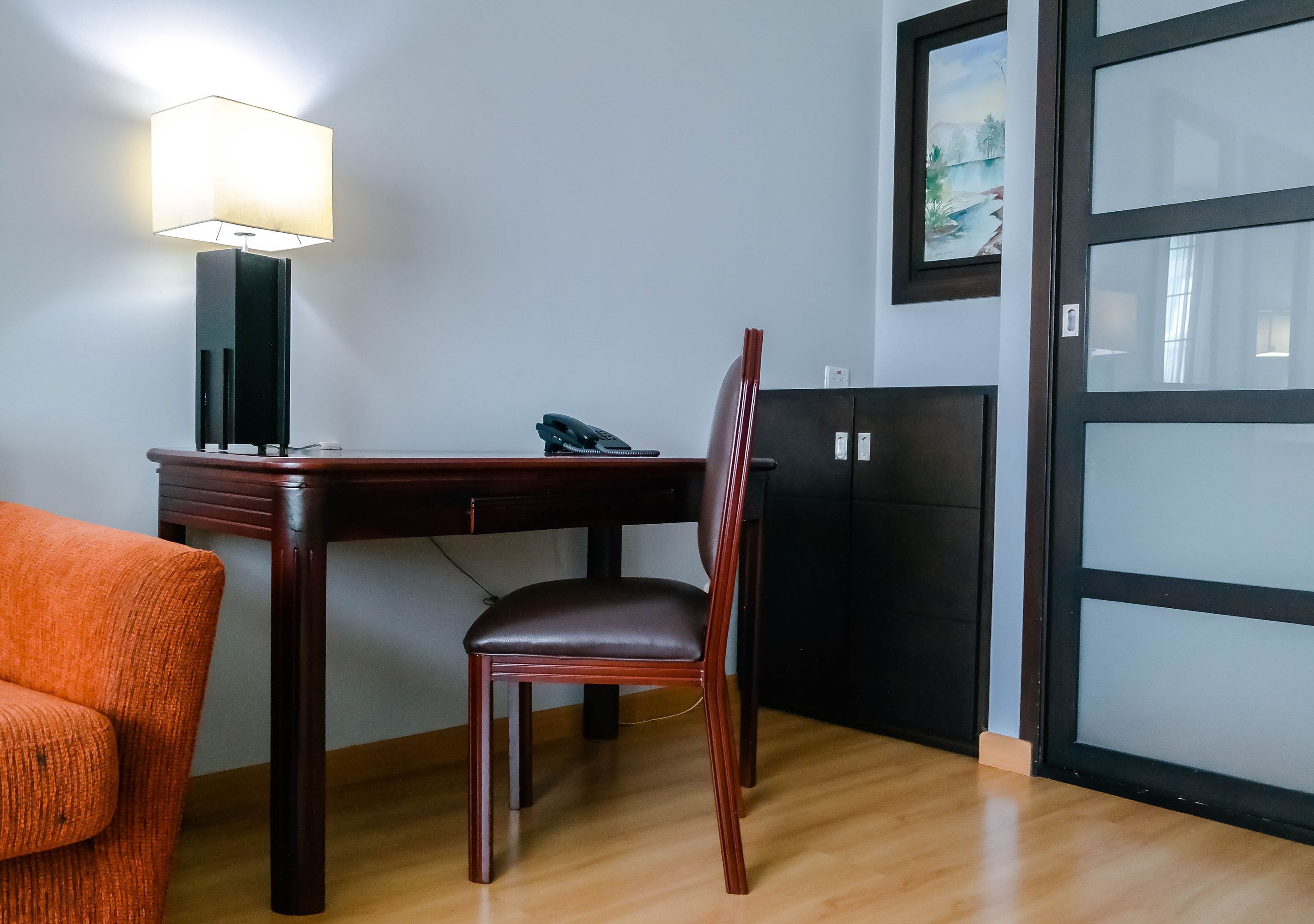 A room with a wooden desk, a chair, a lamp, a telephone, and a cabinet.